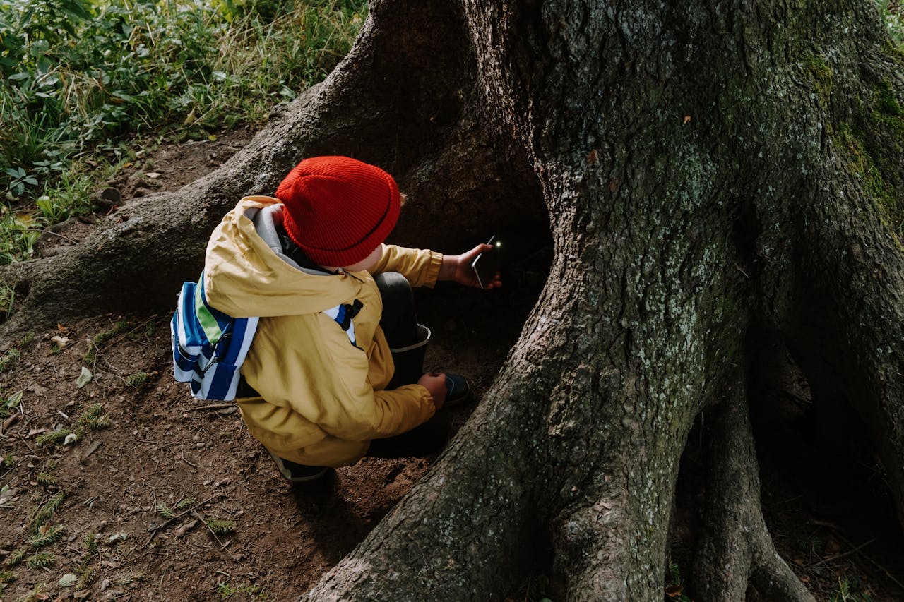 Child exploring outdoors, sitting at tree trunk with a backpack
