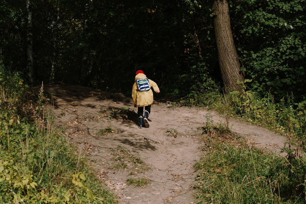 A young child in a yellow jacket runs through a wooded path, embodying autumn adventure.